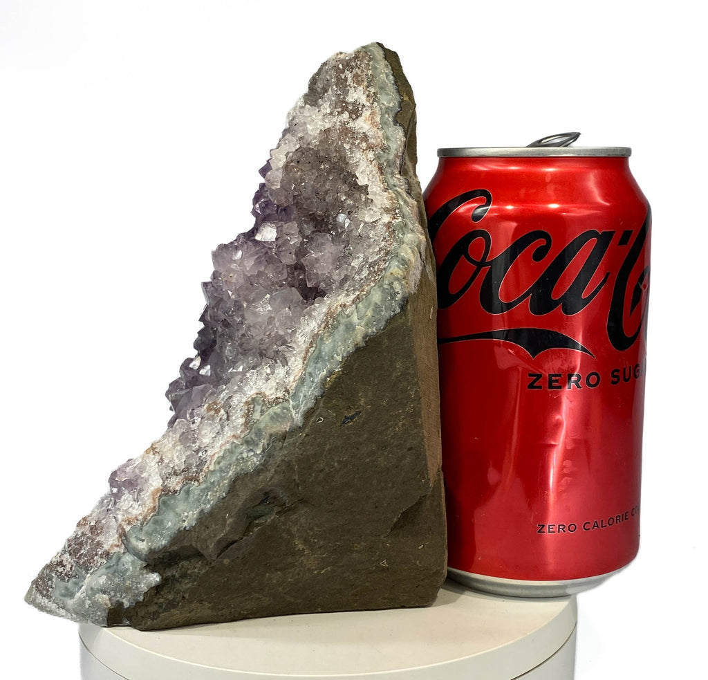 Uruguay amethyst geode with stalactite bumps and lavender crystal flowers, a soda can for scale