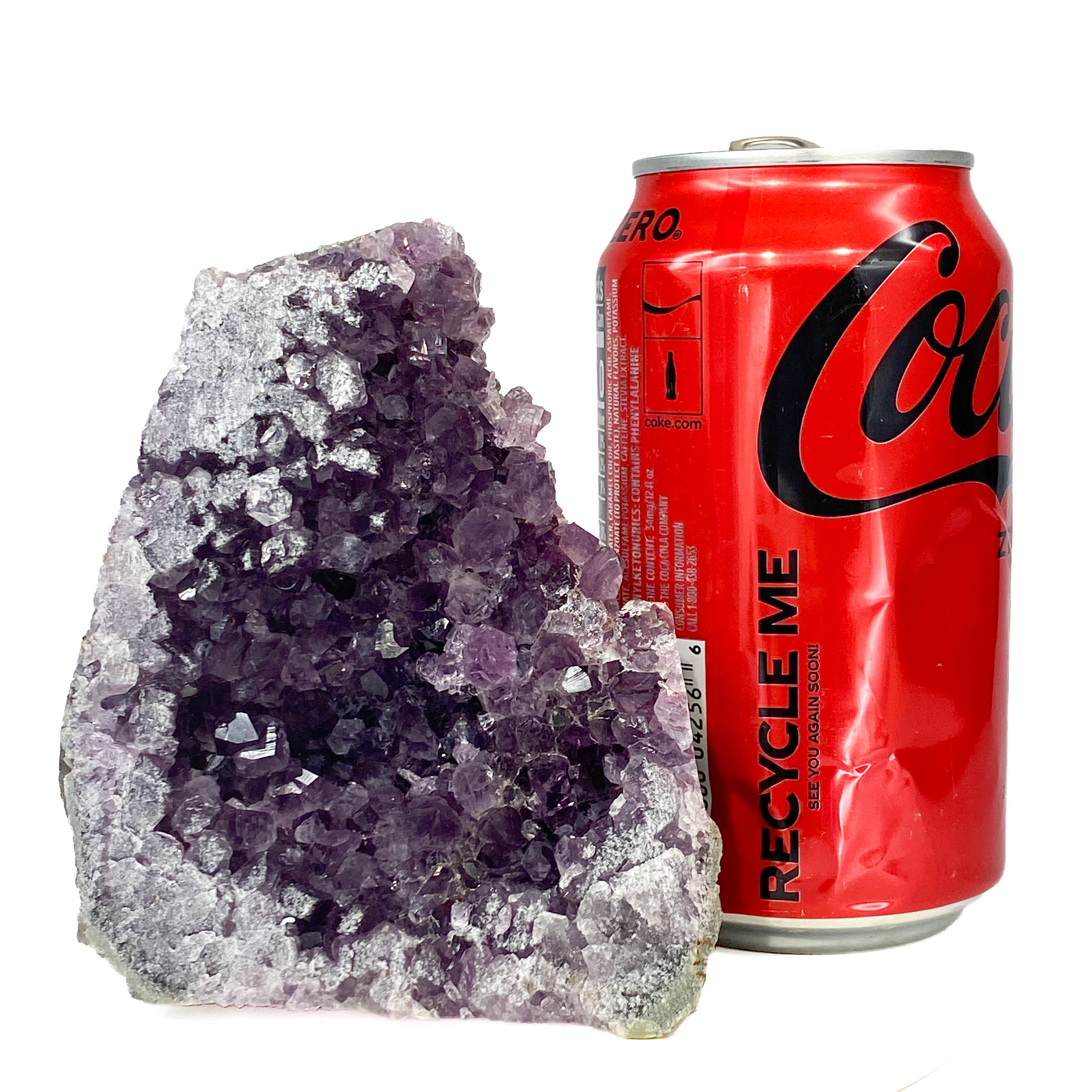 Dark purple amethyst cluster with cross-cut crystal faces, a soda can for scale