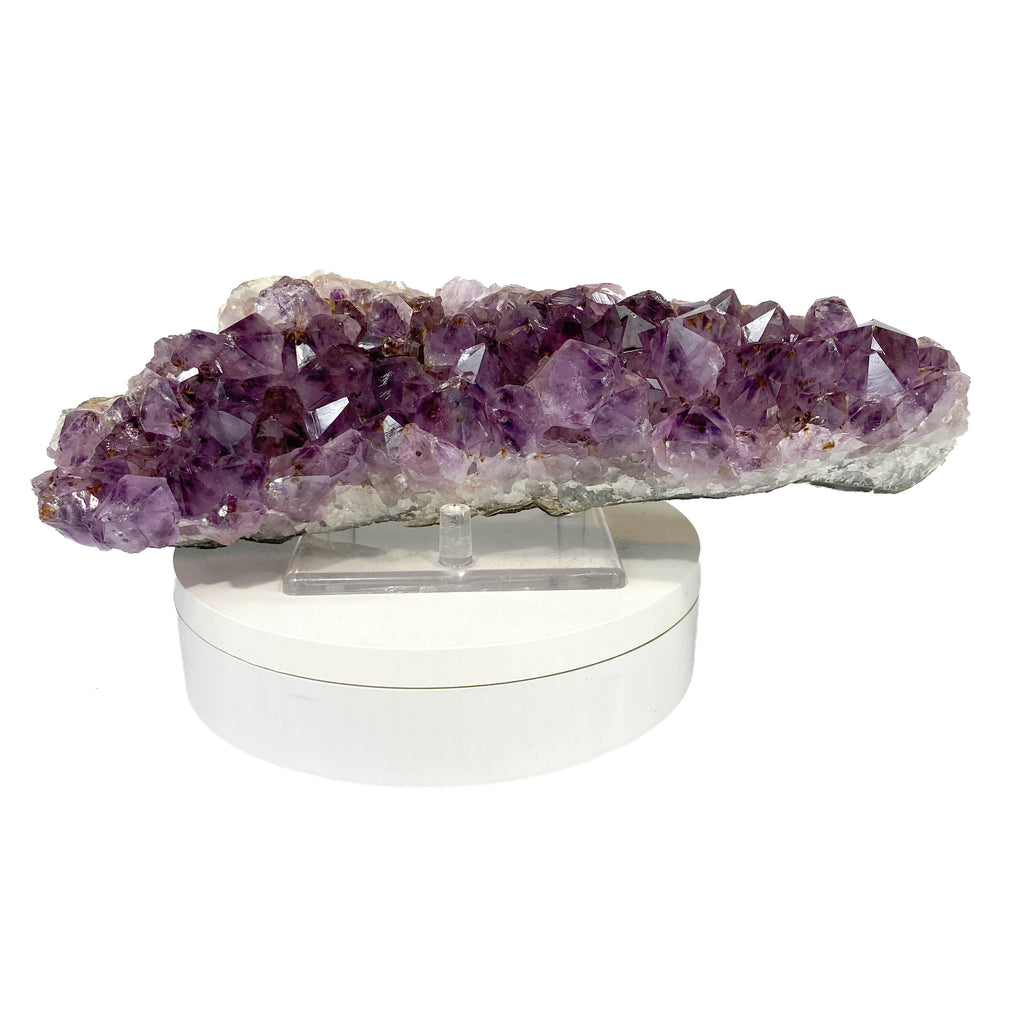 Elongated amethyst cluster with clear, iron-included crystals on white background