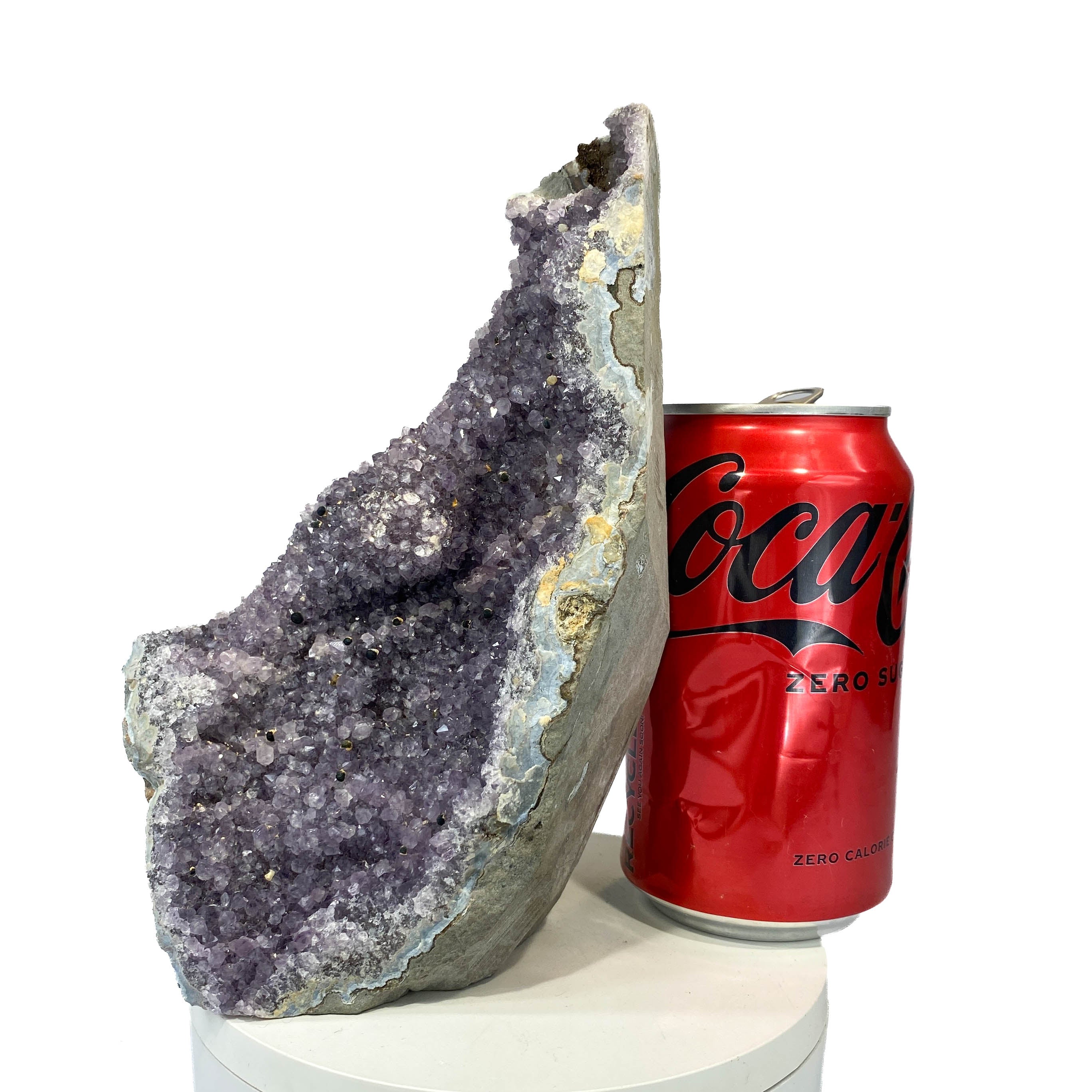 Standing deep amethyst cluster with black nodule inclusions, a soda can for scale