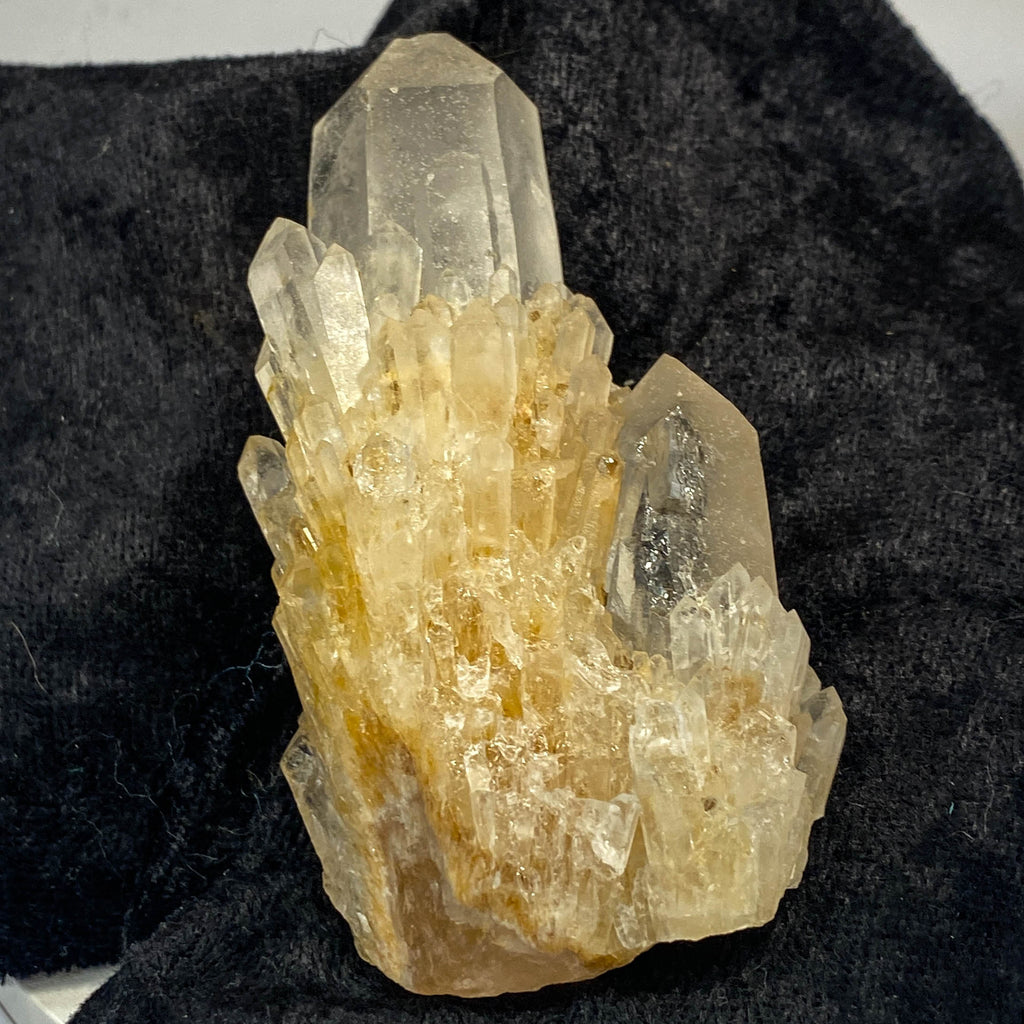 Clear candle quartz crystal cluster with daughter crystals on black cloth background