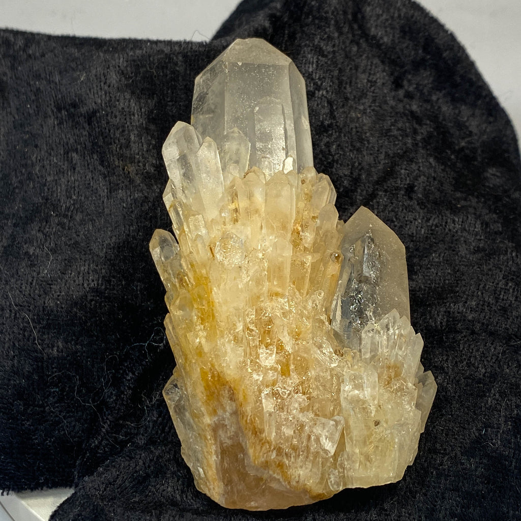 Clear candle quartz crystal cluster with daughter crystals on black cloth background