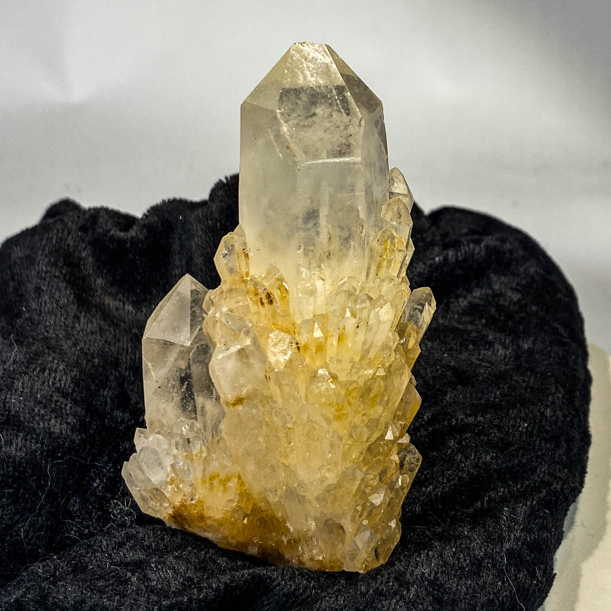 Clear candle quartz crystal cluster with daughter crystals on black cloth background